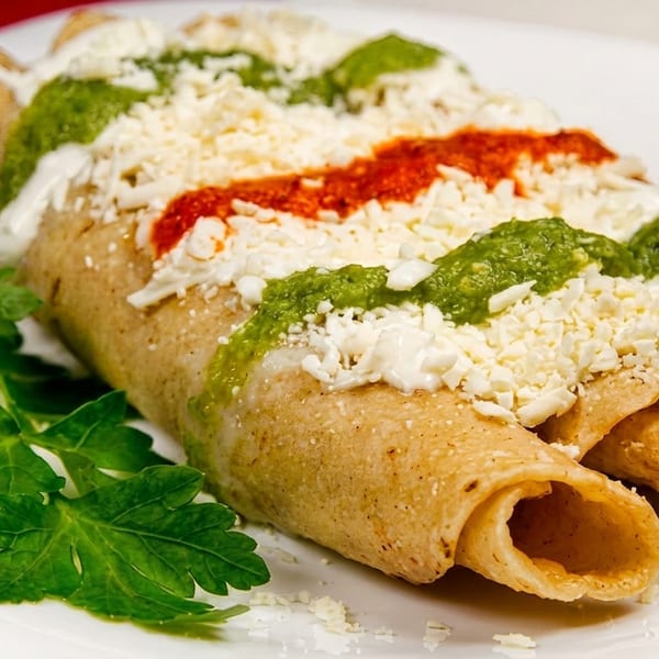 Three golden taquitos topped with green and red sauce, crumbled white cheese, and a parsley garnish.